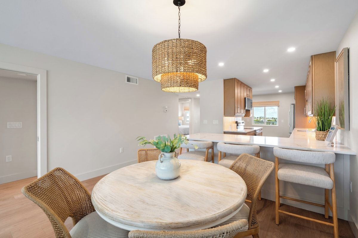 Una cocina moderna con una isla central, sillas de mimbre y un colgador de luz.