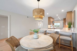 Een moderne keuken met een centraal eiland, rieten stoelen en een hanglamp.