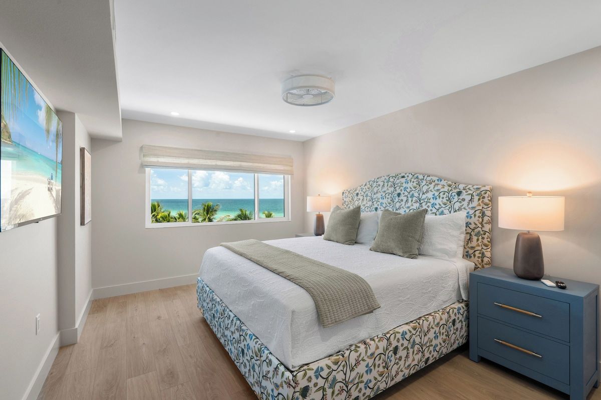 A bedroom with a bed, bedside lamps, a window with a view, and a ceiling fan.
