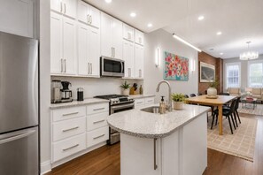 A modern kitchen with white cabinetry, stainless steel appliances, and a central island with a sink. - Walk to TQL | Music Hall Rooftop View | Fire Pit (Cincinnati)