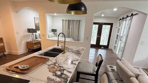 Eine moderne Küche mit einer Marmorinsel, einer schwarzen Pendelleuchte und einem Essbereich mit einer Couch und Stühlen.
