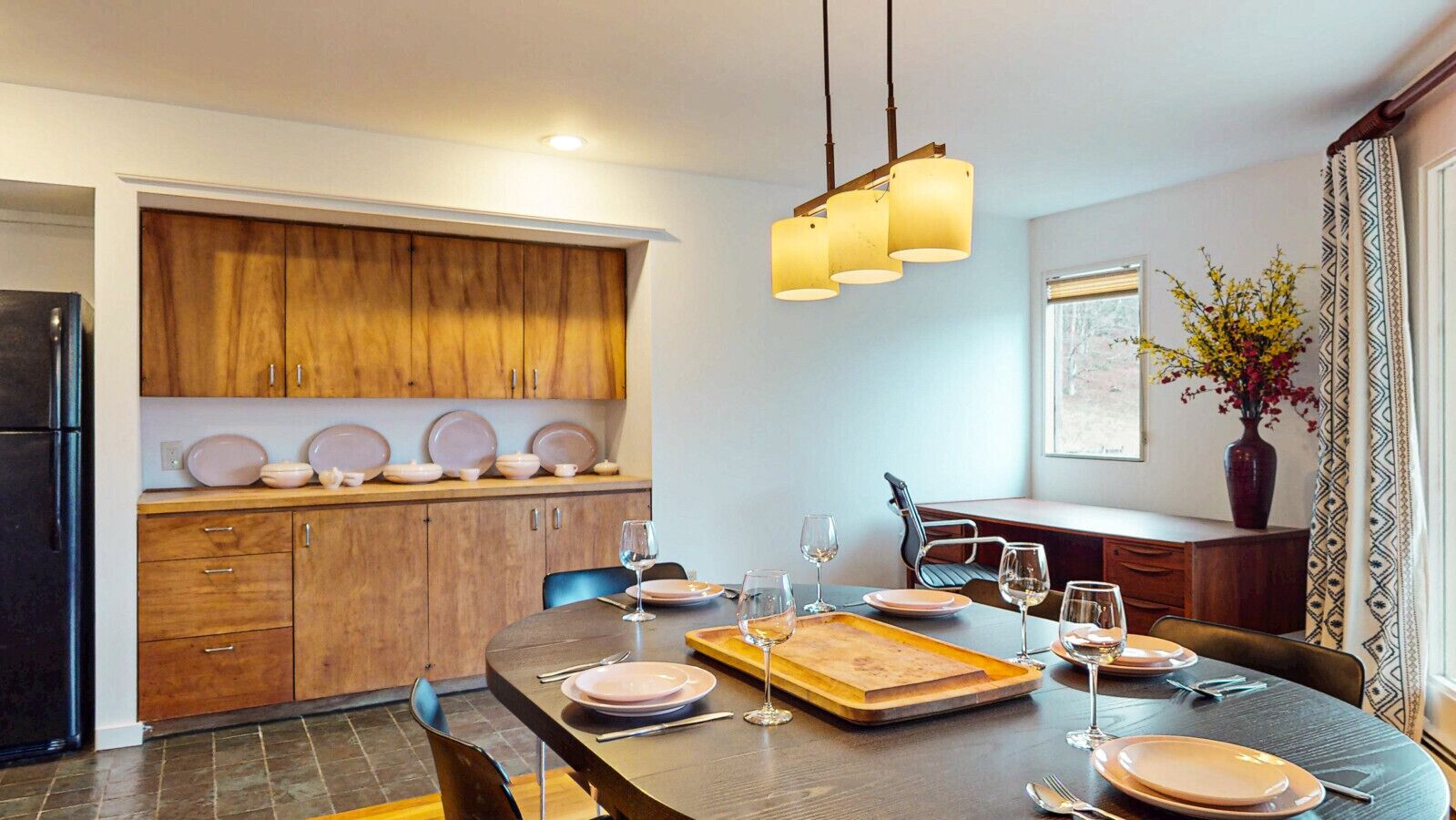 Un coin repas avec une table en bois dressée pour quatre personnes, une cuisine avec des meubles en bois et un luminaire suspendu.