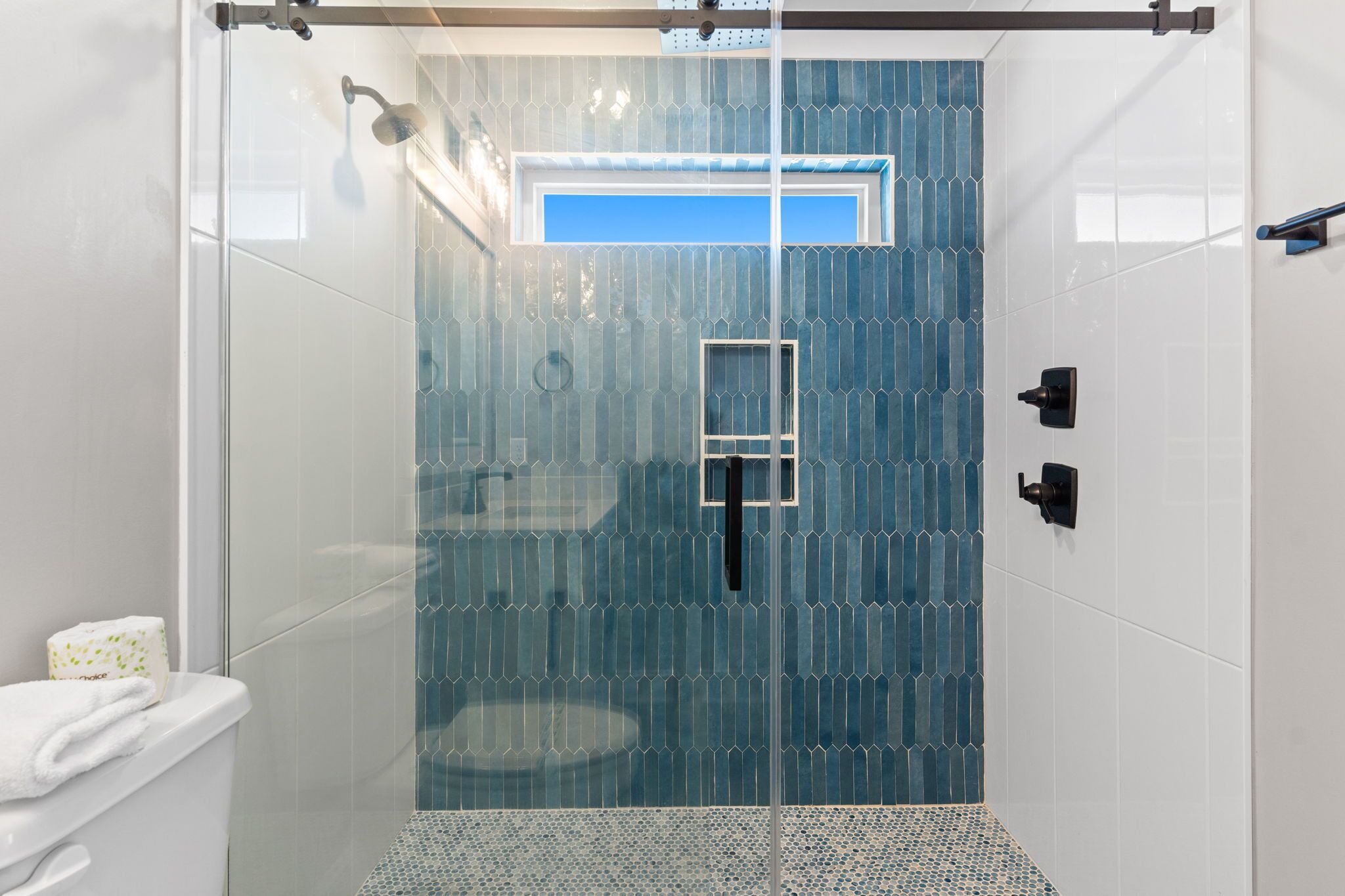 A glass-enclosed shower with a blue-tiled wall, a white toilet, and a towel on the left.