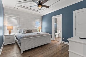 A bedroom with a bed, nightstands, a ceiling fan, a door, and a window. - Weekend Rescue: 10BR 10.5BA, Ocean Views, Pool, Hot Tub, Elevator, Dog Friendly, Sleeps 22 (Oak Island)