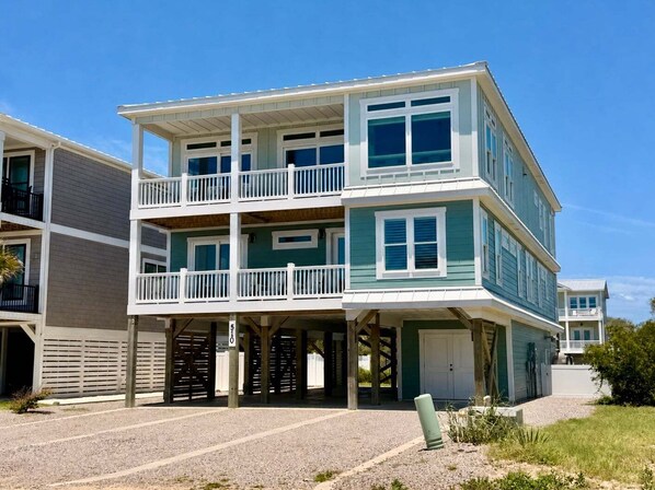 A multi-story beachfront building with balconies, a covered entrance, and a clear sky. - Weekend Rescue: 10BR 10.5BA, Ocean Views, Pool, Hot Tub, Elevator, Dog Friendly, Sleeps 22 (Oak Island)