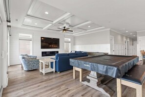 Amplia sala de estar con mesa de billar, sofá azul y ventilador de techo.