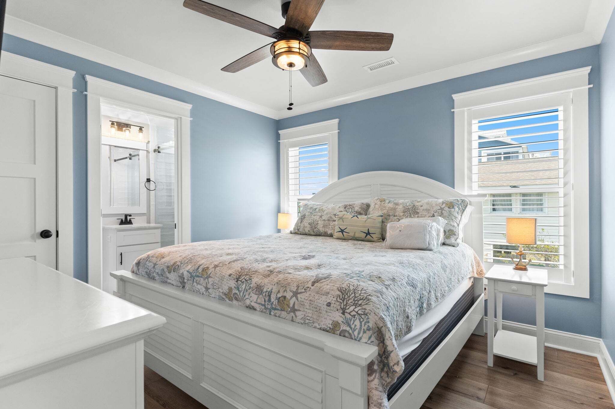 A bedroom with a bed, a vanity, a ceiling fan, and a window with blinds.