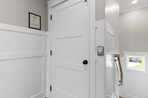 A white door with a black handle, a small window with a view, and a framed notice on the wall. - Weekend Rescue: 10BR 10.5BA, Ocean Views, Pool, Hot Tub, Elevator, Dog Friendly, Sleeps 22 (Oak Island)
