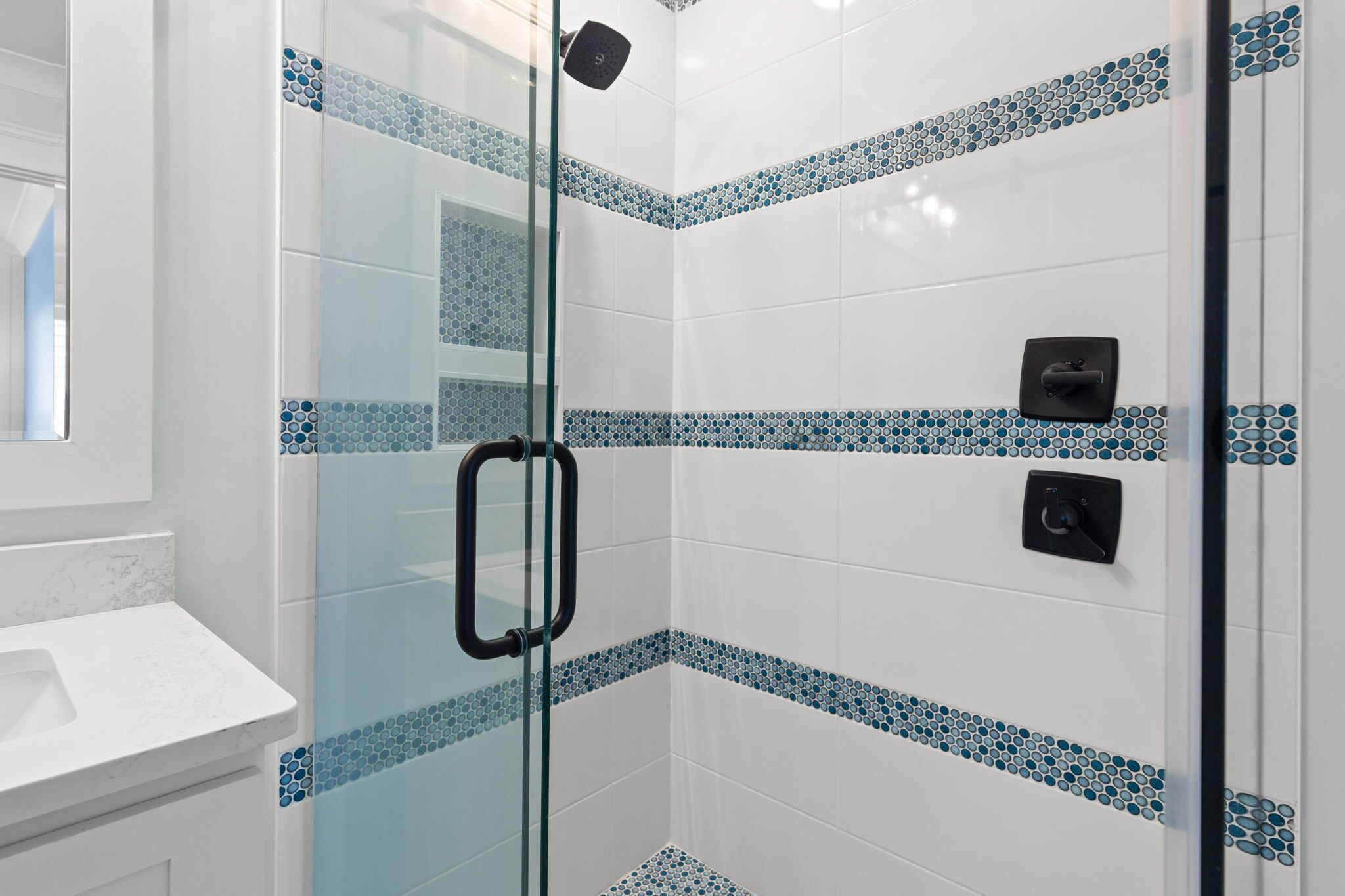 Ducha con puerta de vidrio, paredes de azulejos blancos y detalles decorativos en azul.