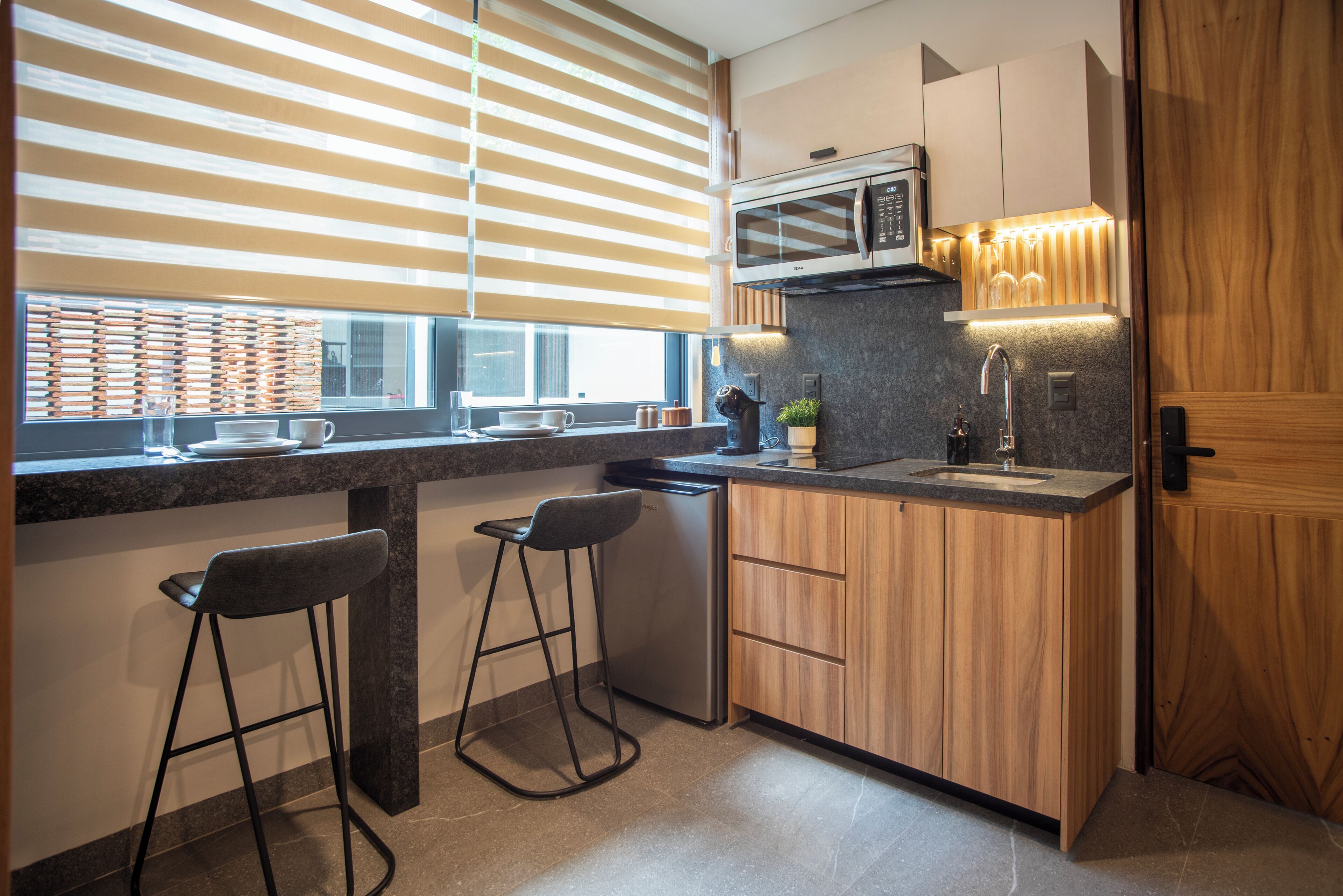 A modern kitchen with a microwave, sink, bar stools, and wooden cabinets.