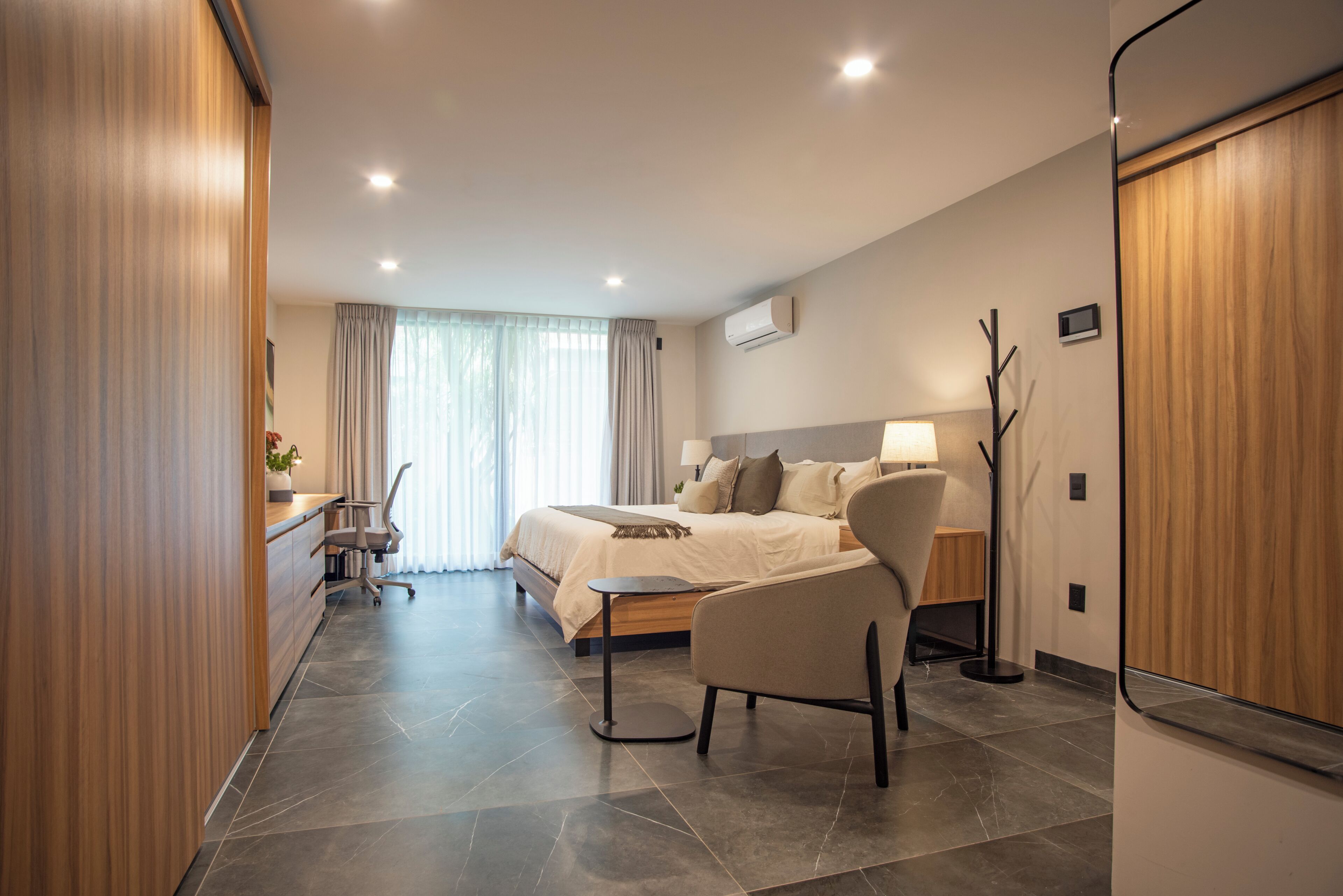 A modern hotel room with a bed, desk, chair, and a large window with curtains.