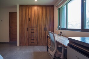 Ein Zimmer mit Holzschrank, Schreibtisch mit Stuhl, Fenster und Küchenzeile.