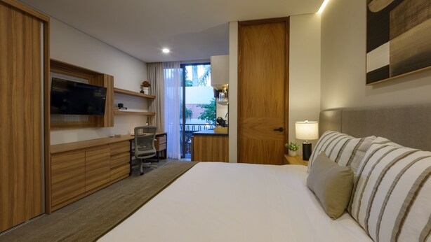A hotel room with a bed, a desk, a TV, and a door leading to a balcony. - Casa Makech (Zapopan)