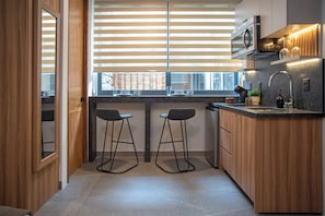 A compact kitchen with wooden cabinets, a built-in microwave, a sink with a modern faucet, and two bar stools.