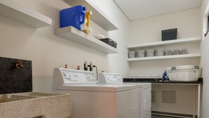 A laundry room with a washing machine, dryer, and shelves with laundry supplies. - Casa Makech (Zapopan)