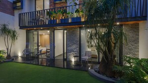 A modern two-story house with a balcony, a glass door entrance, and a small patio area with chairs and a table. - Casa Makech (Zapopan)