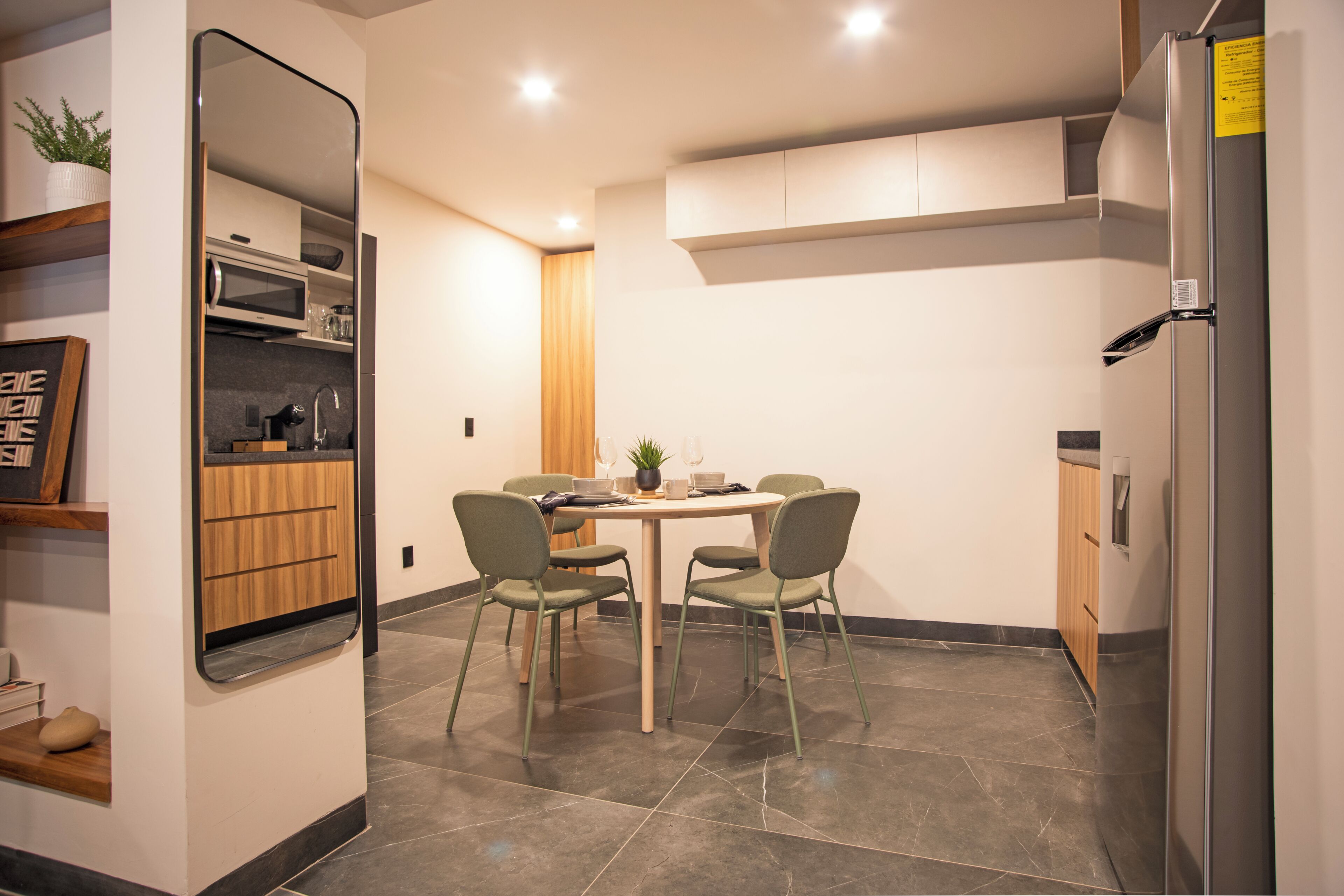 A compact kitchen with a dining table, chairs, a microwave, and a refrigerator.