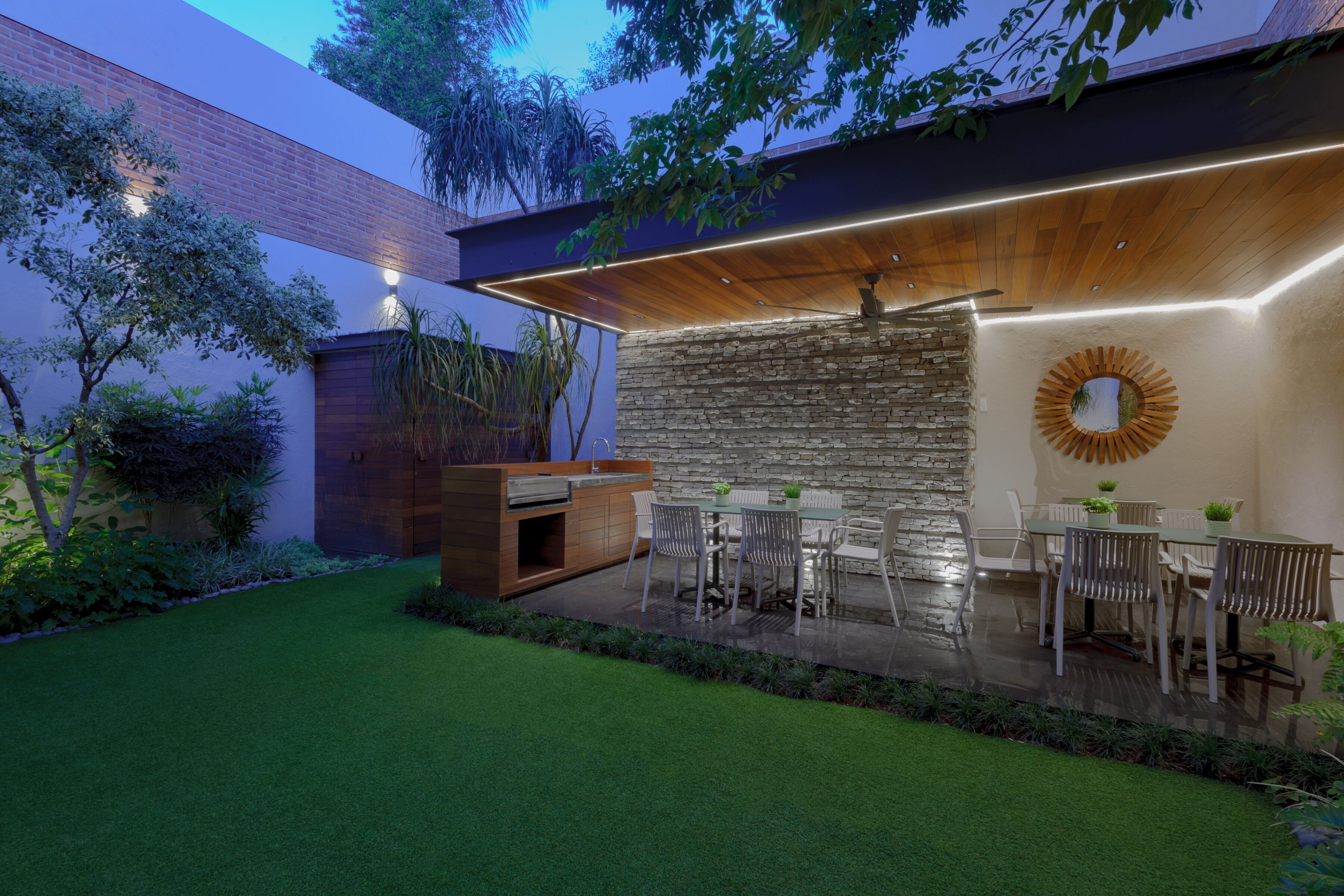Un patio moderno al aire libre con pared de piedra, techo de madera y zona de comedor con sillas y una mesa.