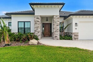 A modern house with a stone facade, a front door, and a garage. - Sunset Riverfront House 4BR | Heated Pool, Hot Tub + Outdoor Kitchen ☀️ (Cocoa Beach)