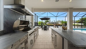 Eine moderne Küche mit integriertem Grill, Stein-Arbeitsplatten und Blick auf einen Swimmingpool.