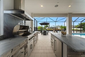 Eine moderne Küche mit integriertem Grill, Stein-Arbeitsplatten und Blick auf einen Swimmingpool.
