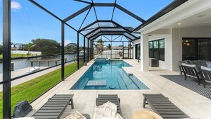 Ein moderner Poolbereich im Freien mit Glasverkleidung, Liegestühlen und Blick auf einen Fluss.