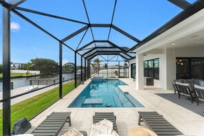 Ein moderner Poolbereich im Freien mit Glasverkleidung, Liegestühlen und Blick auf einen Fluss.