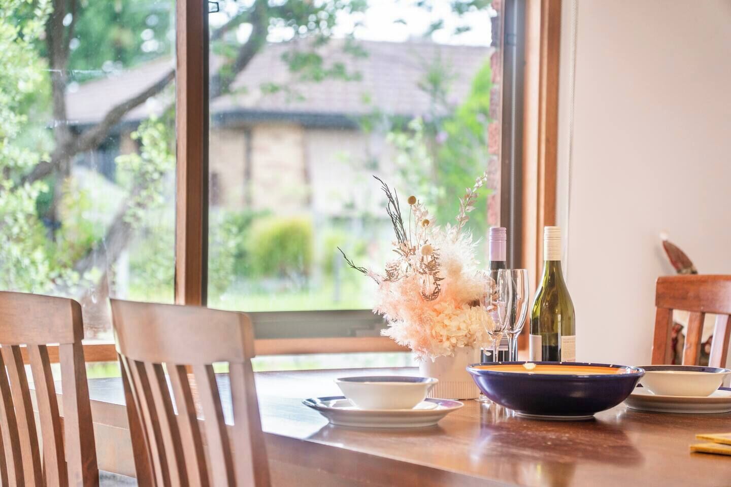 Une table à manger avec des chaises, un vase de fleurs, des bouteilles de vin et des verres.