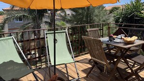 Uma varanda com mesa e cadeiras de madeira, e um guarda-sol amarelo.