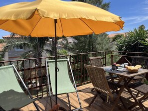 Ein Balkon mit Holztisch, Stühlen und einem gelben Sonnenschirm.