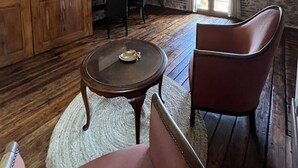 Um quarto com parede de pedra, assoalho de madeira, televisão fixada na parede, uma mesa de jantar com cadeiras e um armário de madeira grande.