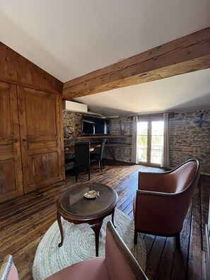 Ein Zimmer mit Steinwand, Holzboden, einem an der Wand montierten Fernseher, einem Esstisch mit Stühlen und einer großen Holzkassette.