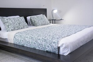 A bed with a patterned bedspread, a bedside table with a lamp, and a dark headboard. - HOSTAL SANTA BARBARA (SANTO DOMINGO)