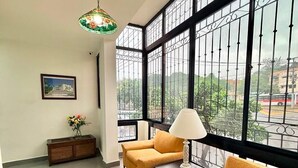 Una habitación con ventanas amplias, un sofá, una mesa, una lámpara y un cuadro en la pared.