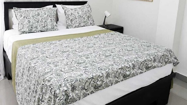 Un dormitorio con una cama, cortinas blancas, una lámpara de noche y un cuadro en la pared.