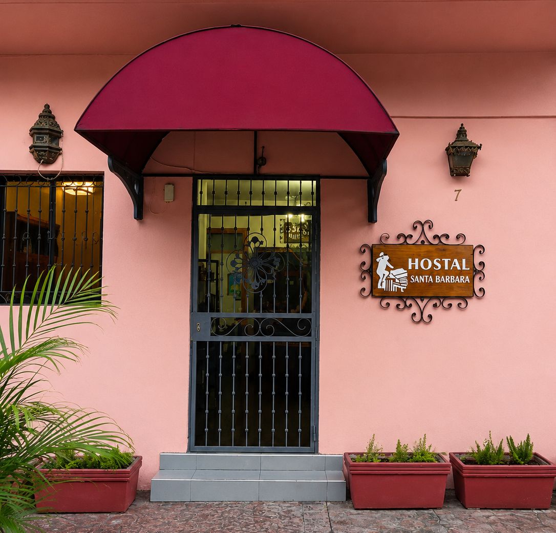 Un edificio rosa con una verja negra, plantas en macetas y un letrero que dice 'HOSTAL SANTA BARBARA'.