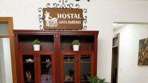 Un mostrador de recepción con un monitor Planar, una silla de oficina negra, un mueble de madera con puertas de cristal y un letrero que dice 'HOSTAL SANTA BARBARA'.