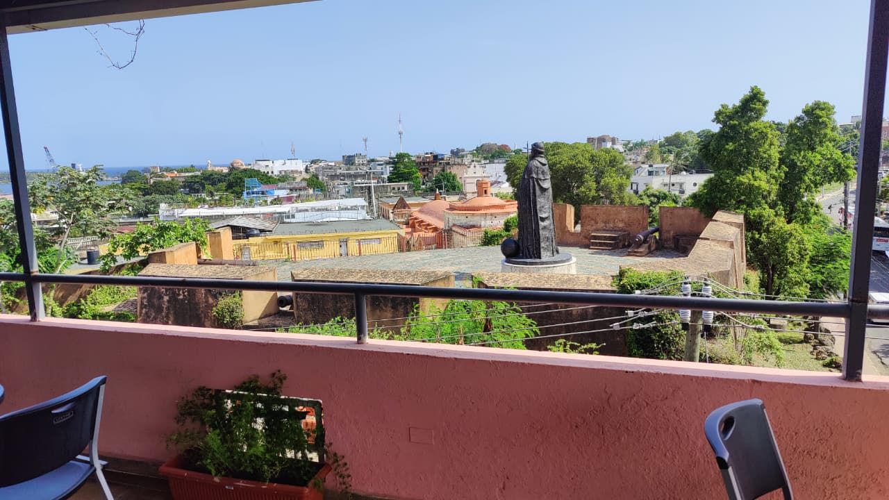 Un balcón con vistas a un paisaje urbano, que incluye edificios y una estatua.