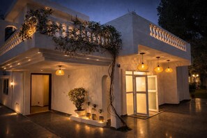 A modern building with a covered entrance, potted plants, and hanging lights. - Charming 4-bedroom air conditioned bungalow with Pool in South Delhi (Delhi)