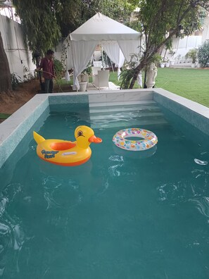 Una piscina con juguetes inflables, una carpa blanca y plantas en macetas.