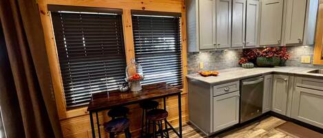 Une cuisine avec des murs en bois, des meubles gris, un coin bar avec des tabourets et un panneau indiquant : « HEURE LOCALE DE LA MONTAGNE ».
