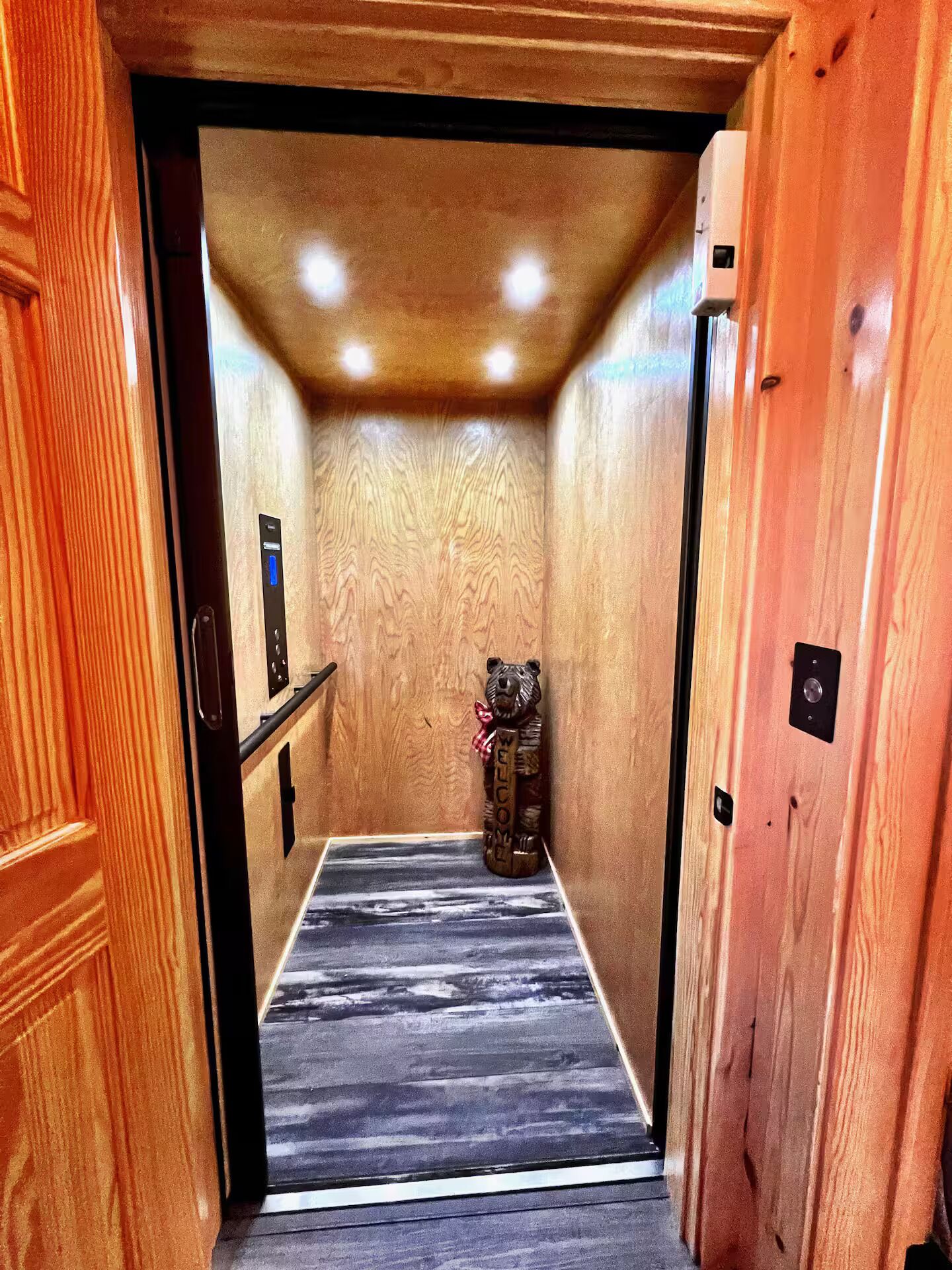 Een houten elevatorinterieur met een beersymbool, een bedieningspaneel en een decoratieve wand.