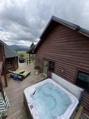 Een houten hut met een jacuzzi, terrasstoelen en uitzicht op bergen.