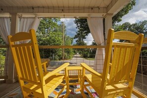 Un espace extérieur aménagé avec des sièges, protégé par un toit, comprenant des chaises jaunes et une table, et offrant une vue sur un sentier et la verdure.