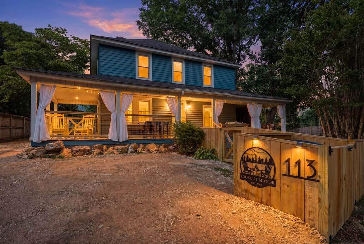 A two-story house with a porch, a wooden fence with a number, and a sign indicating the property name.
