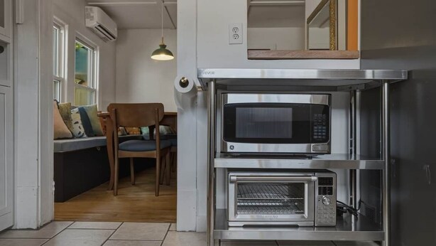 Uma cozinha compacta com micro-ondas e forno embutidos, uma cadeira de madeira e uma luminária pendente.