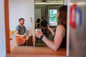Un coin repas avec une table et des chaises, une personne tenant un verre et une porte-fenêtre donnant sur une autre pièce.