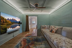 Un salon doté d’un téléviseur à écran plat, d’un ventilateur de plafond, d’un canapé agrémenté de coussins à motifs et d’un tapis aux couleurs vives.