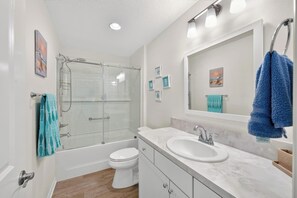 Une salle de bain moderne avec une douche à parois de verre, des toilettes blanches, un lavabo avec un miroir et un porte-serviettes avec des serviettes bleues.