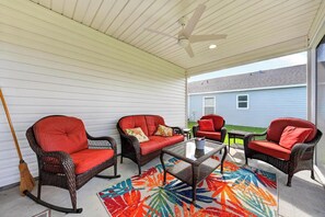 Eine überdachte Terrasse mit Korbmöbeln, einem Besen und einem farbenfrohen Teppich.